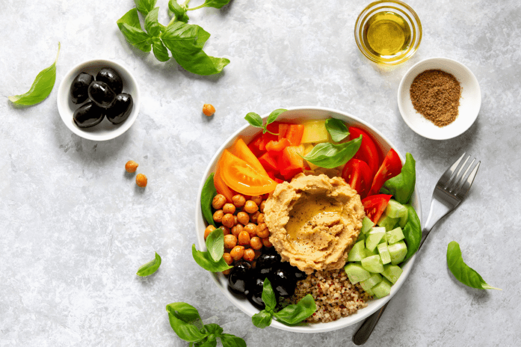 Healthy chicken and veggie meal prep bowl with quinoa, corn, fresh greens, and colorful vegetables on a light background