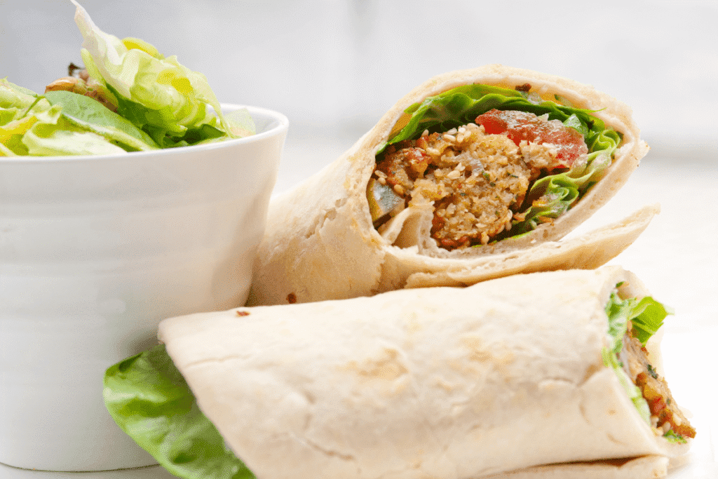 Fresh Mediterranean vegan chickpea wrap with lettuce, tomatoes, and herbs served on a white plate