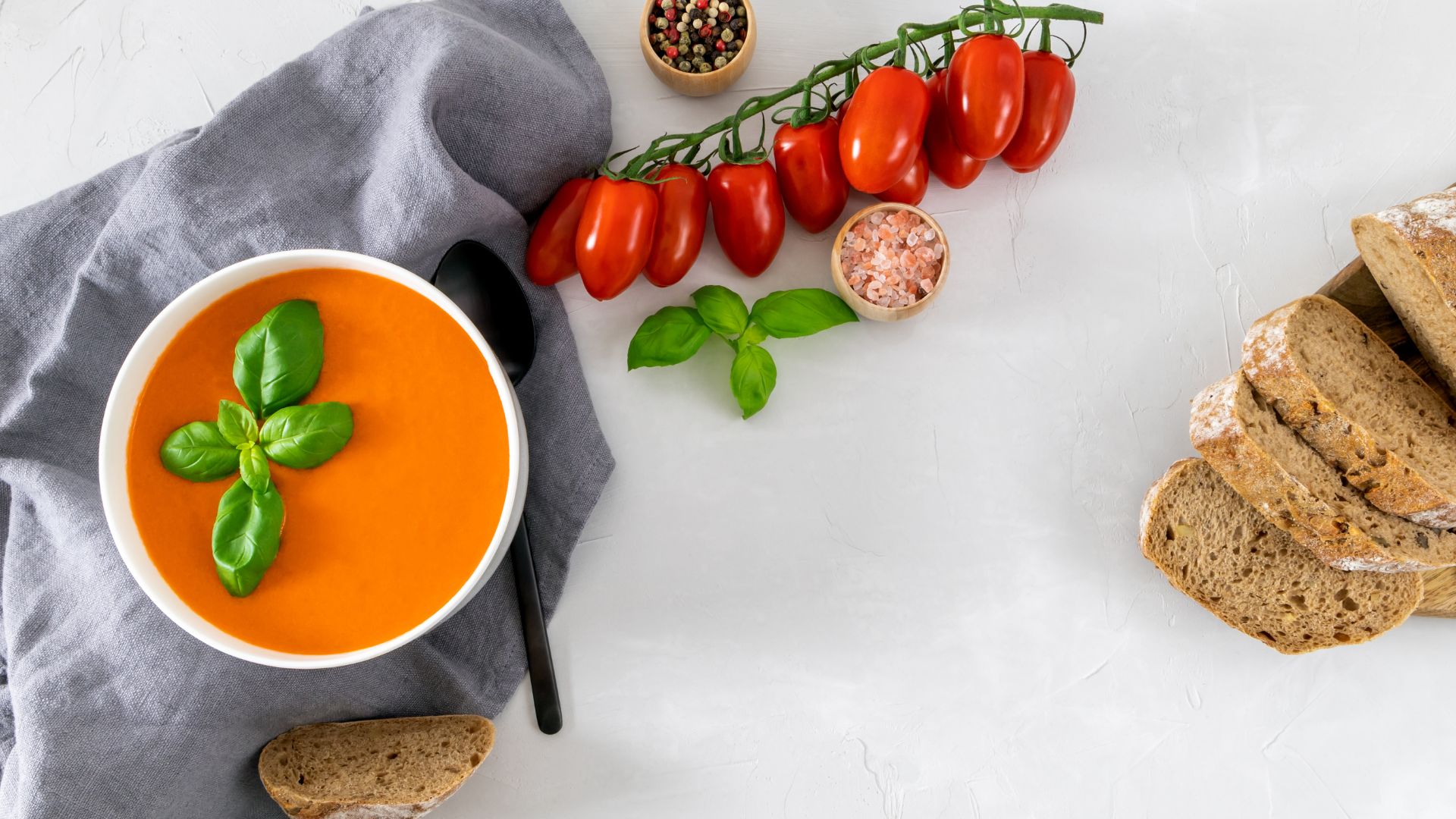11 Vegan tomato soup recipe - creamy dairy-free soup in bowl with fresh basil, crusty bread on rustic table