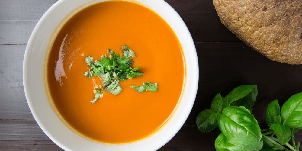 Homemade plant-based tomato soup in white bowl with garnish