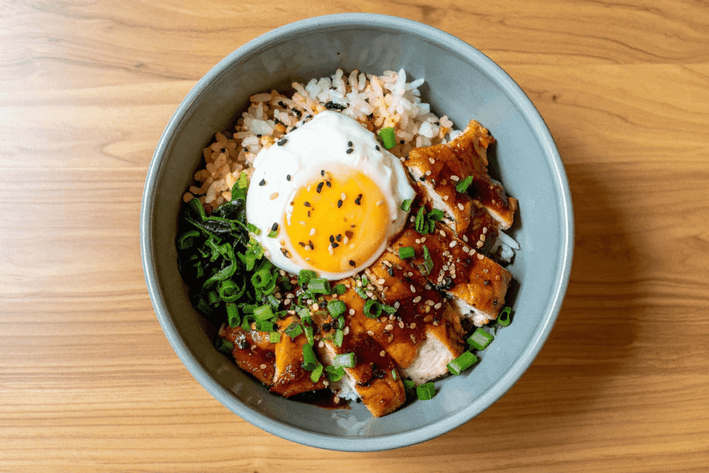 Asian-inspired chicken and rice meal prep bowl with sautéed vegetables and a fried egg on a wooden background