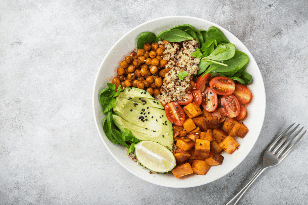 Colorful vegan Buddha bowl with roasted sweet potatoes, chickpeas, quinoa, fresh spinach, avocado slices, and cherry tomatoes