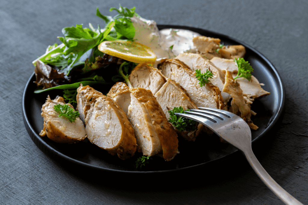Sliced grilled chicken served with fresh greens in a black bowl, healthy high-protein meal