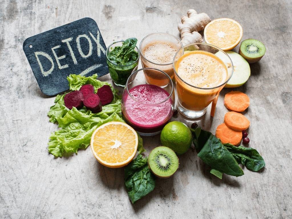 Fresh detox ingredients with colorful juices: ginger, kiwi, spinach, citrus, beets, and carrots
