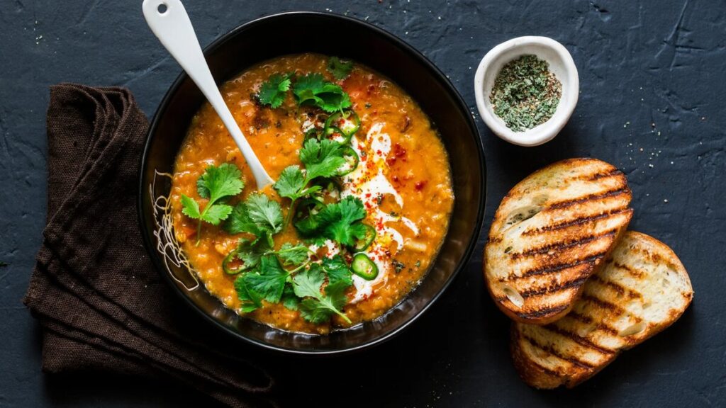 Warming vegan red lentil curry soup with coconut milk, cilantro, and grilled bread in a black bowl