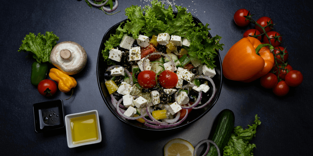 A fresh, vibrant salad featuring colorful tomatoes, bell peppers, cucumbers, and lettuce, topped with plant-based cheese and served in a large bowl.
