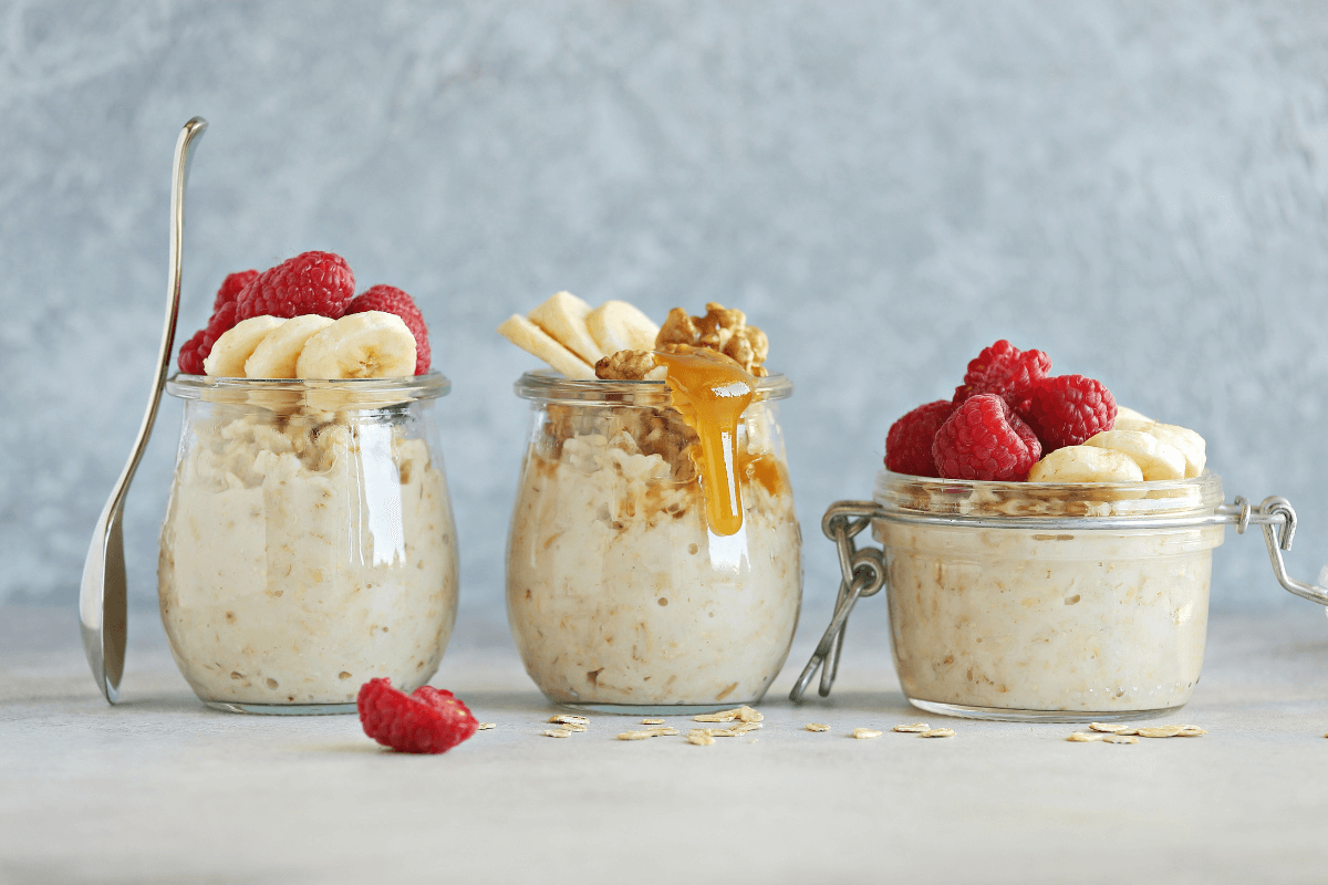 2 (1) Three glass jars of mixed berry cheesecake overnight oats topped with banana, raspberries, and honey – a healthy no-bake breakfast idea.