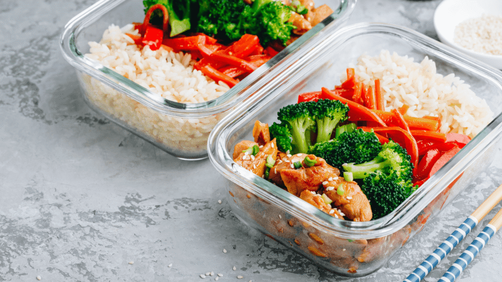 High-protein meal prep containers with rice, grilled chicken, broccoli, and red bell peppers in clear glass containers for storage and reheating.