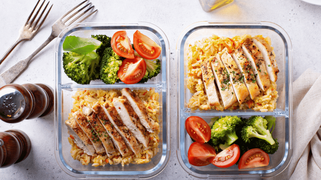 High-protein chicken meal prep containers with brown rice, broccoli, and cherry tomatoes