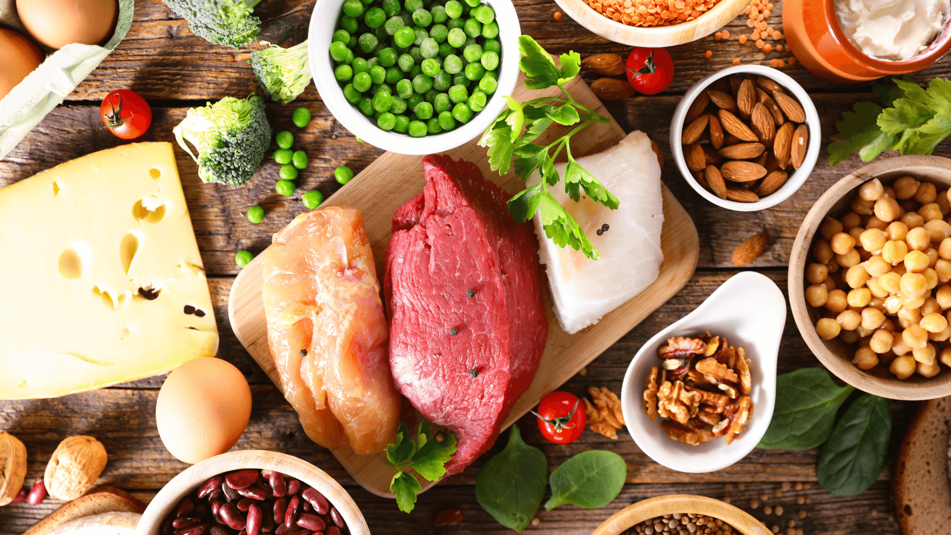 A variety of high-protein foods including lean beef, chicken breast, chickpeas, cheese, and green vegetables.