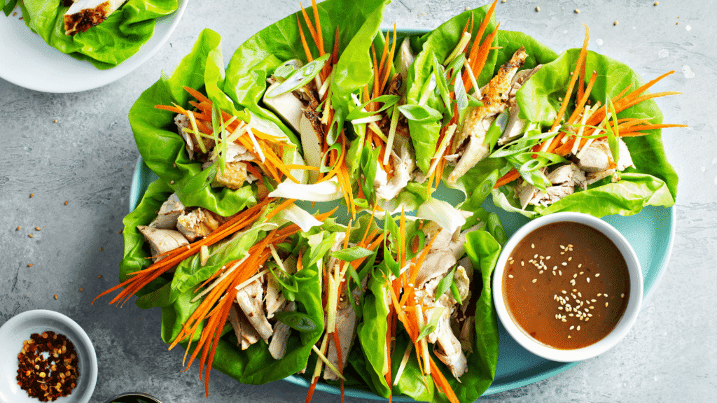 Low-carb chicken lettuce wraps with shredded carrots, romaine leaves, and sesame dipping sauce – healthy and satisfying