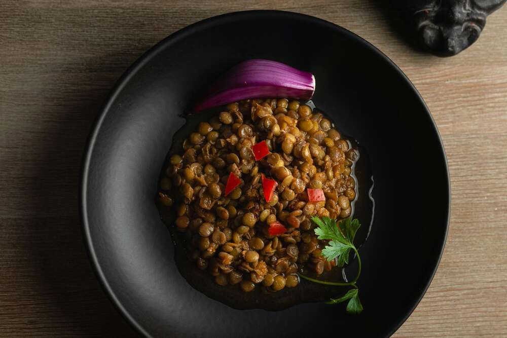 Cooked lentils with red pepper and onion in a dark bowl, high protein plant based food
