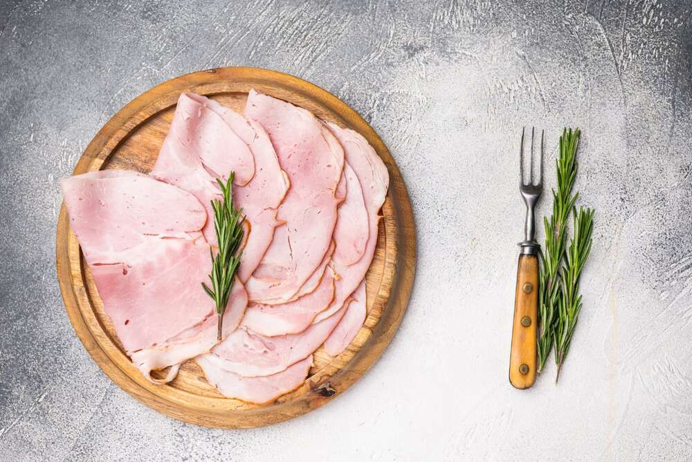
Thin sliced turkey breast on wooden board with rosemary and fork, high protein deli meat