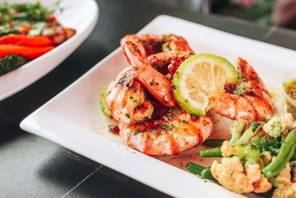 Grilled shrimp with lemon and vegetables on a white plate, high protein seafood