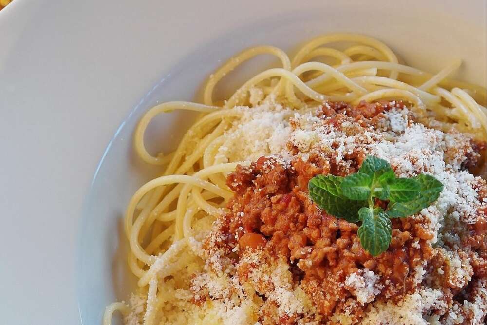 Lentil bolognese sauce over spaghetti pasta with parmesan shavings and fresh basil in white bowl