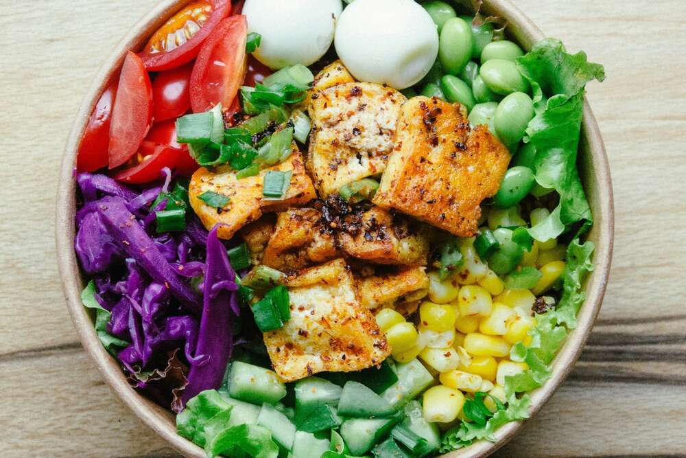 Crispy tofu bowl with edamame, tomatoes, corn and purple cabbage, high protein plant based meal