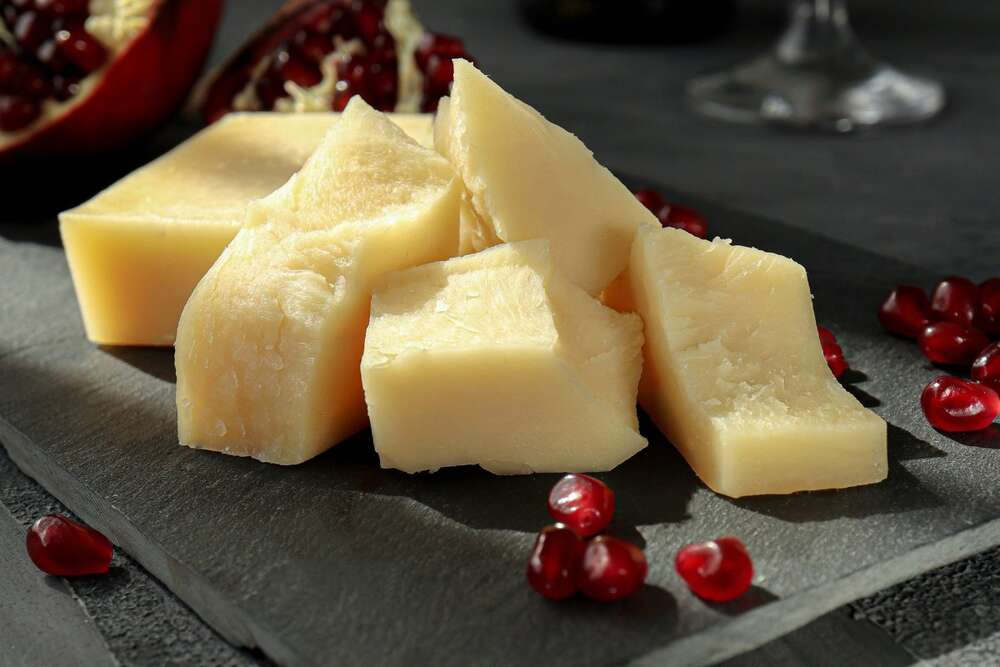 Parmesan cheese pieces on dark slate board with pomegranate seeds, high protein cheese