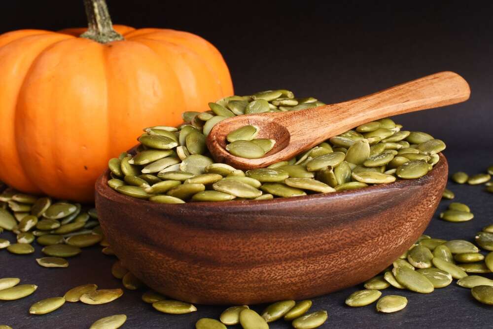 Pumpkin seeds in wooden bowl with whole pumpkin, high protein healthy snack