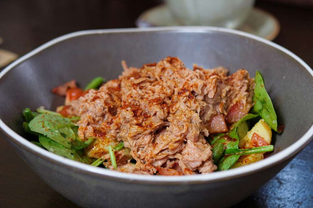 Canned tuna with green vegetables in a dark bowl, high protein food