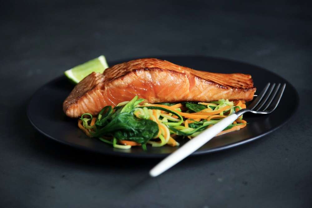 Grilled salmon fillet with green vegetables on a dark plate, high protein food