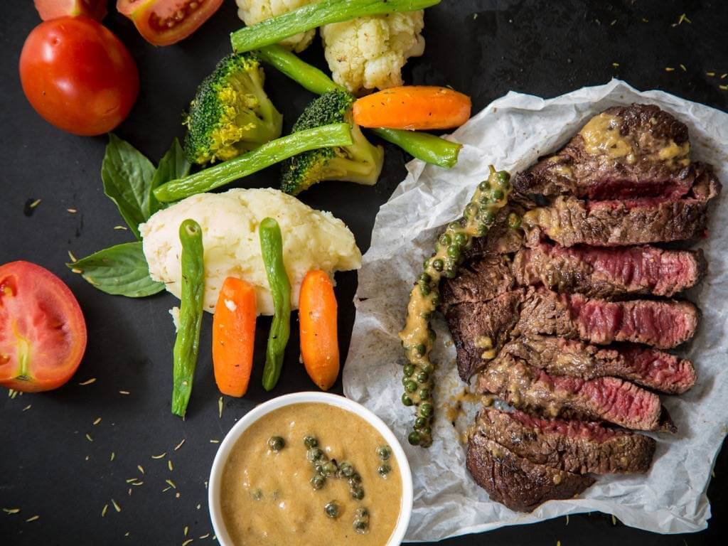 Sliced grilled steak with colorful steamed vegetables and a creamy dipping sauce – a balanced high-protein dinner idea.