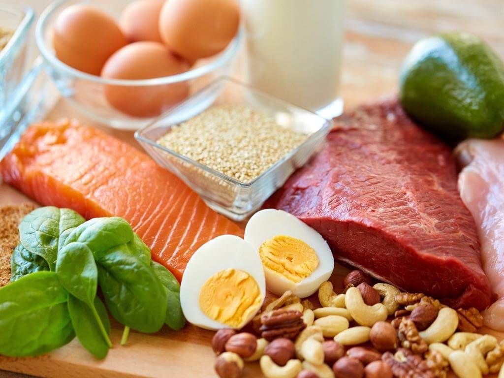 High-protein foods including salmon, eggs, beef, and nuts on a wooden table – perfect for healthy meal prep.