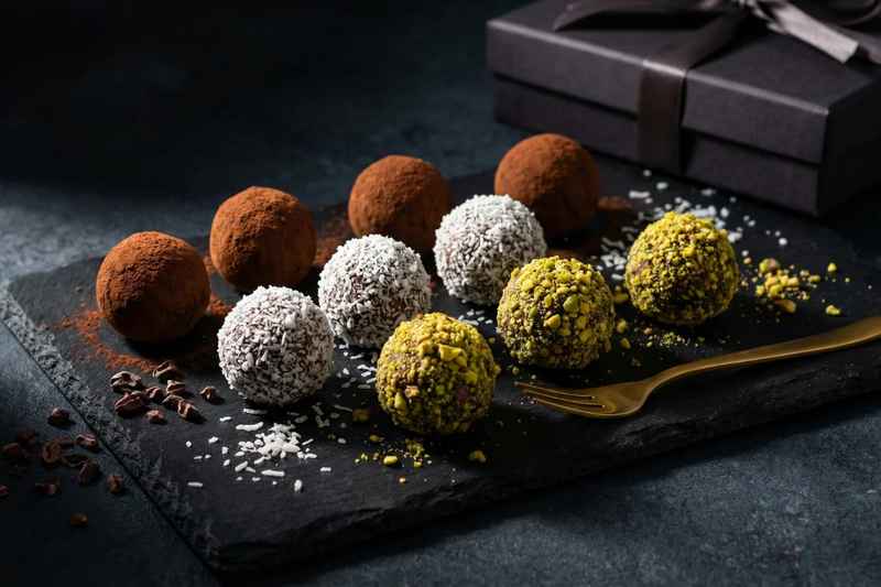 Assortment of raw vegan chocolate truffles coated in cacao, coconut, and crushed nuts on slate board