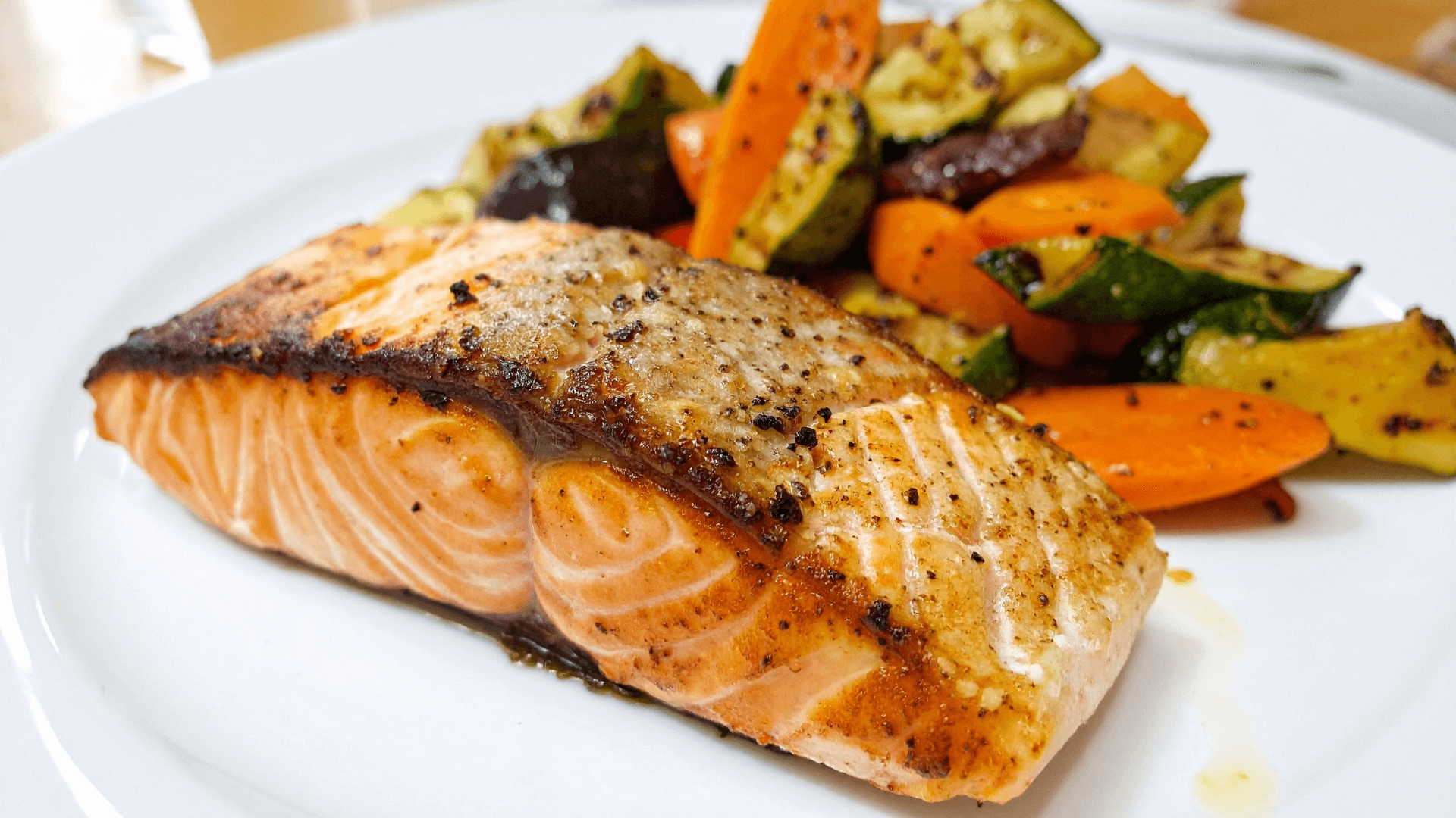 Mediterranean baked salmon fillet with crispy skin served with roasted zucchini, carrots and bell peppers on white plate