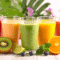 Colorful healthy fruit smoothies with kiwi, orange, and berries displayed outdoors on a bright natural background
