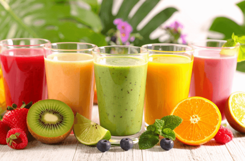 Colorful healthy fruit smoothies with kiwi, orange, and berries displayed outdoors on a bright natural background