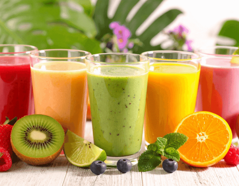 Colorful healthy fruit smoothies with kiwi, orange, and berries displayed outdoors on a bright natural background