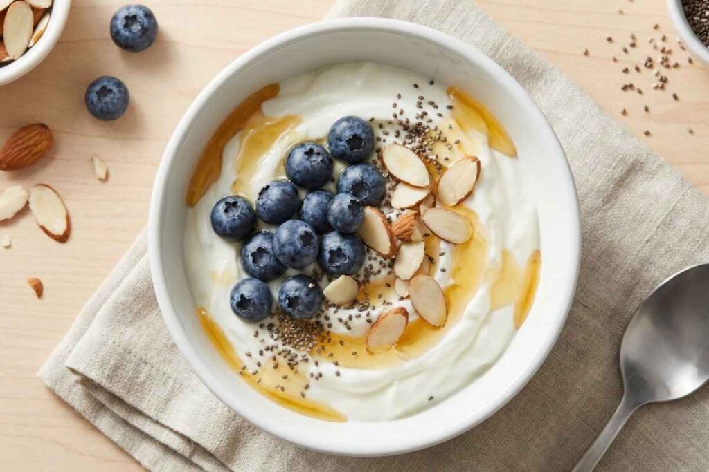 High protein Greek yogurt bowl topped with almonds, chia seeds, flax seeds, and fresh blueberries - 28g protein healthy snack idea
