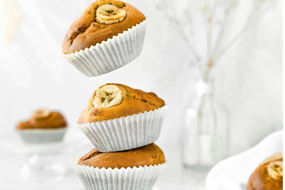 Banana nut protein muffins meal prep stacked with walnuts on white background