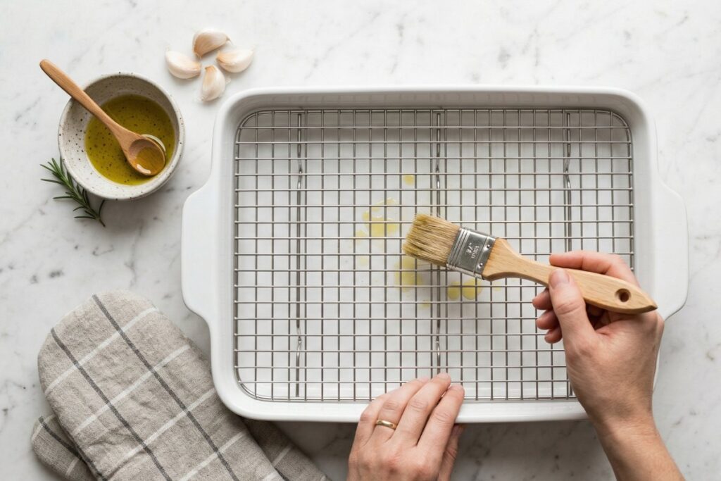 Brushing a wire rack in a white baking dish with olive oil 
to prepare for baked chicken thighs
